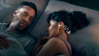 A couple in bed. The woman has dark hair tied in a bun and is wearing Philips Sleep Headphones