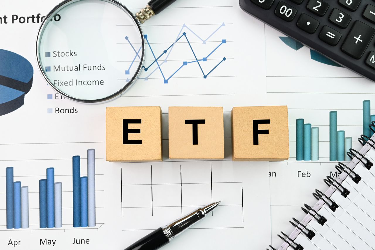 Wooden blocks show the letters E T F on top of notepads covered in charts and financial data