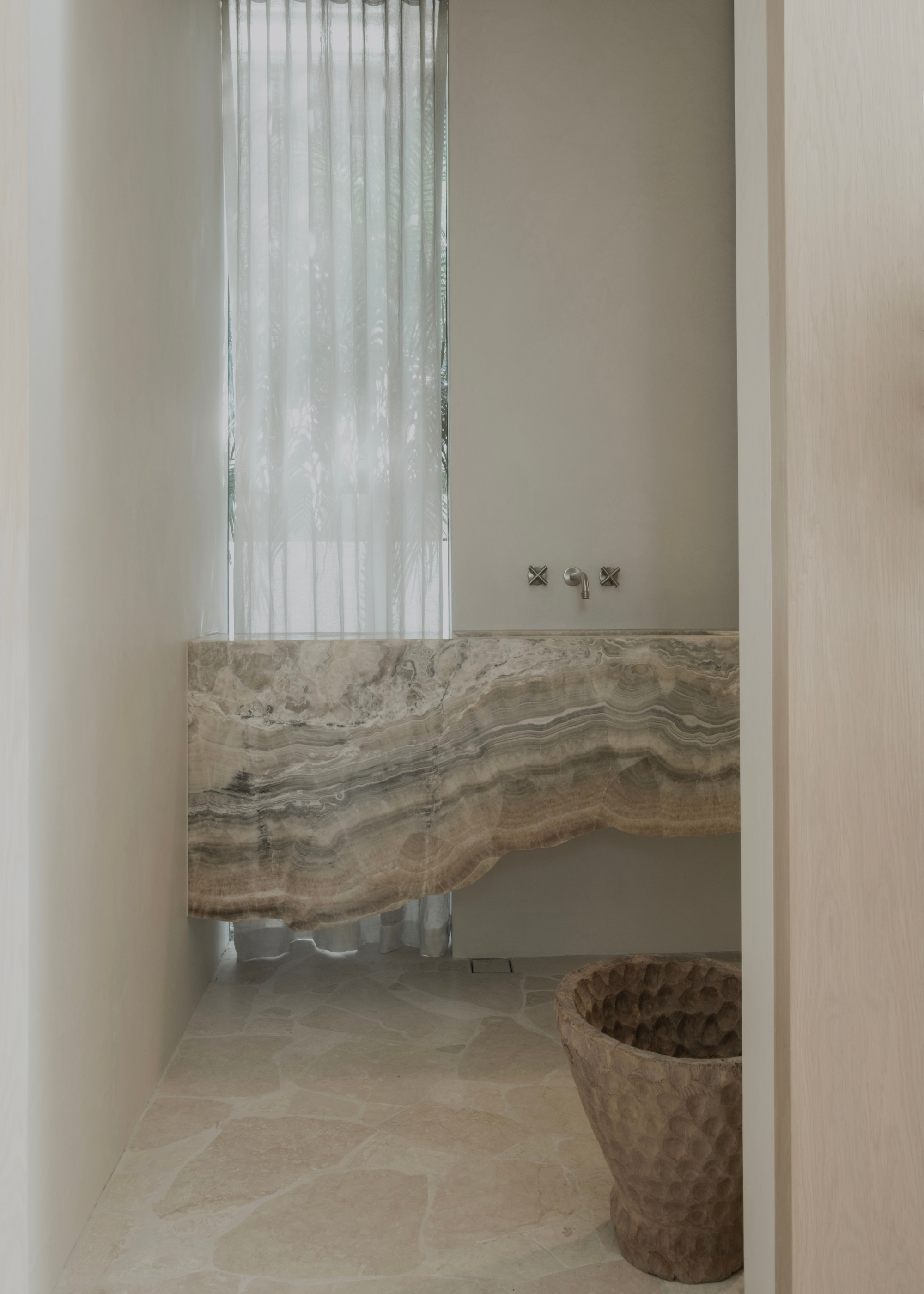 A stone bathroom sink in a white room with a textured basket