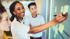 Agile development concept image showing office workers during a brainstorming session placing sticky notes on a board.