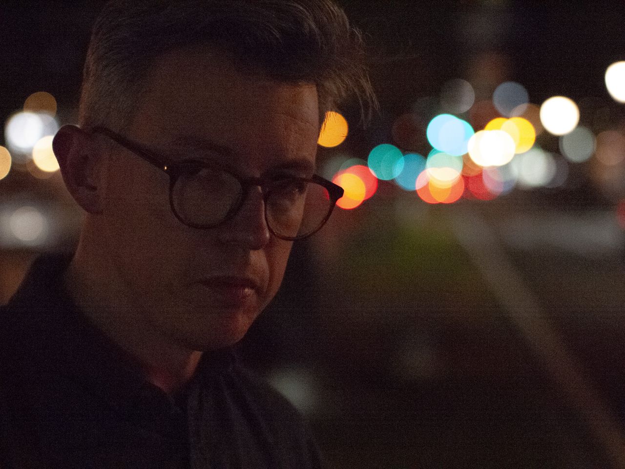 Portrait of a man at night in a city, there are blurred circular light behind him, shot with the Panasonic Lumix G1