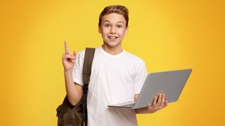A smiling child holding a laptop and schoolbag on a yellow background.