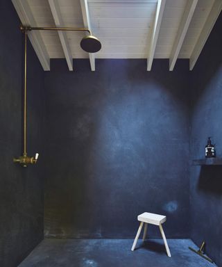 A wet room with blue finish, brass shower, stool, and white wood beamed ceiling