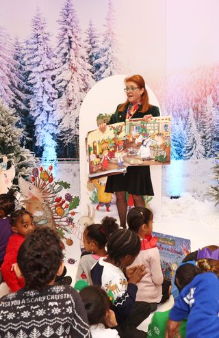 Sarah Ferguson wstanding in front of a snow-covered backdrop reading a large illustrated book to a crowd of kids