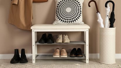 A bench with shoe storage beneath beside an umbrella stand and under hanging coats