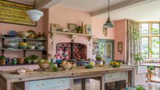 unfitted kitchen in manor house with antique cooks table, pink walls and Aga