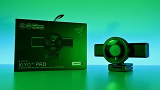 Razer Kiyo V2 Pro webcam with its privacy shutter closed, resting next to its retail box on a green-lit surface.