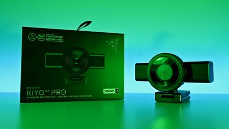 Razer Kiyo V2 Pro webcam with its privacy shutter closed, resting next to its retail box on a green-lit surface.