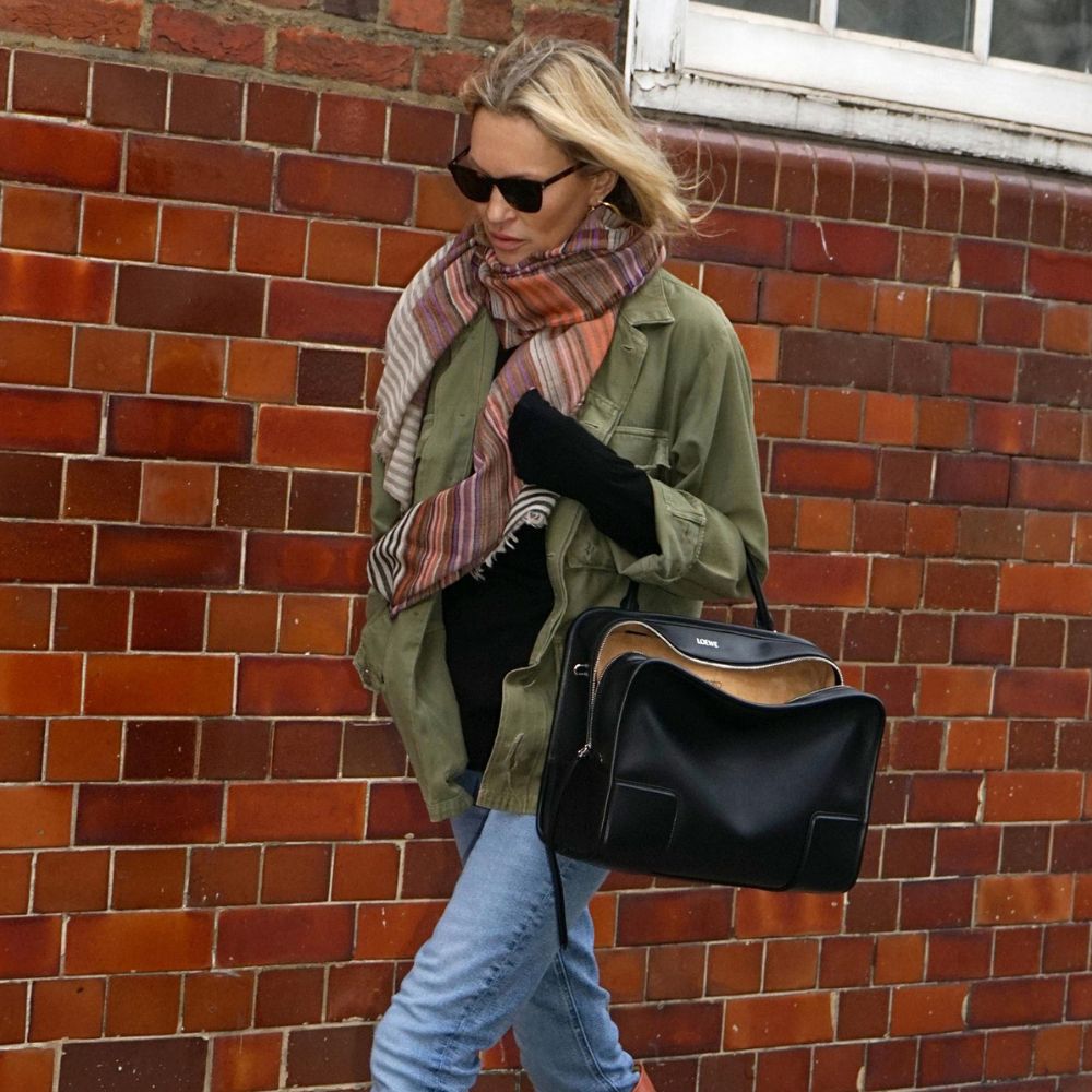Kate Moss walks down the street wearing skinny jeans and knee-high boots with a khaki jacket and oversized scarf.