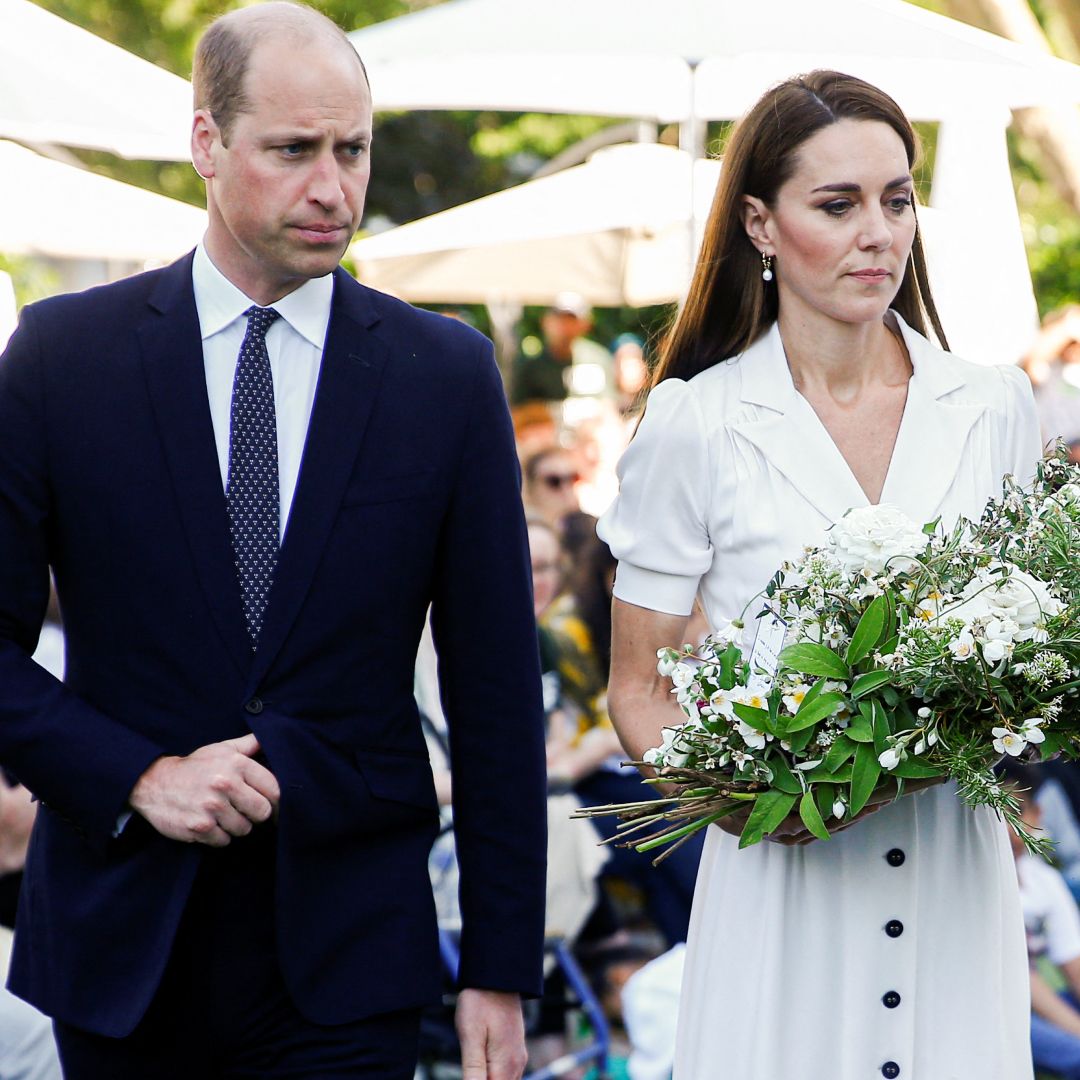 Prince William wears a suit and looks stern while Kate Middleton wears a white dress and carries a large bouquet of white flowers