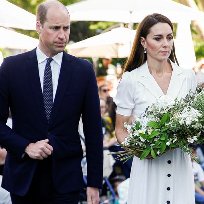 Prince William wears a suit and looks stern while Kate Middleton wears a white dress and carries a large bouquet of white flowers