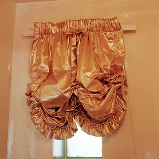 A curtain made of orange satin handing off the window in a room with yellow walls