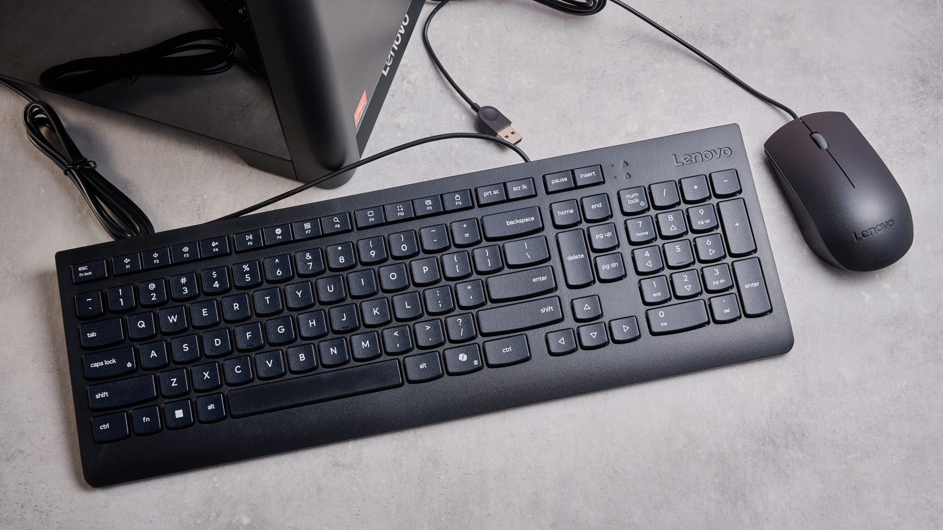 Birds-eye view of black mouse and keyboard and bottom portion the Lenovo Legion Tower 5, on a grey desk