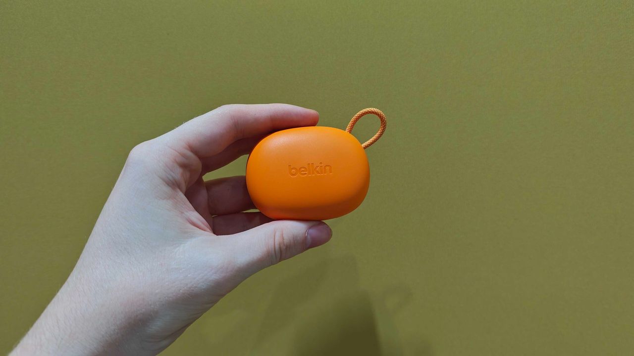 Belkin SoundForm Isolate Buds in orange and in a man's hand, with a wooden table in the background