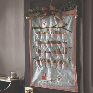 A reusable fabric advent calendar hung on the back of a door decorated with eucalyptus foliage and a bow