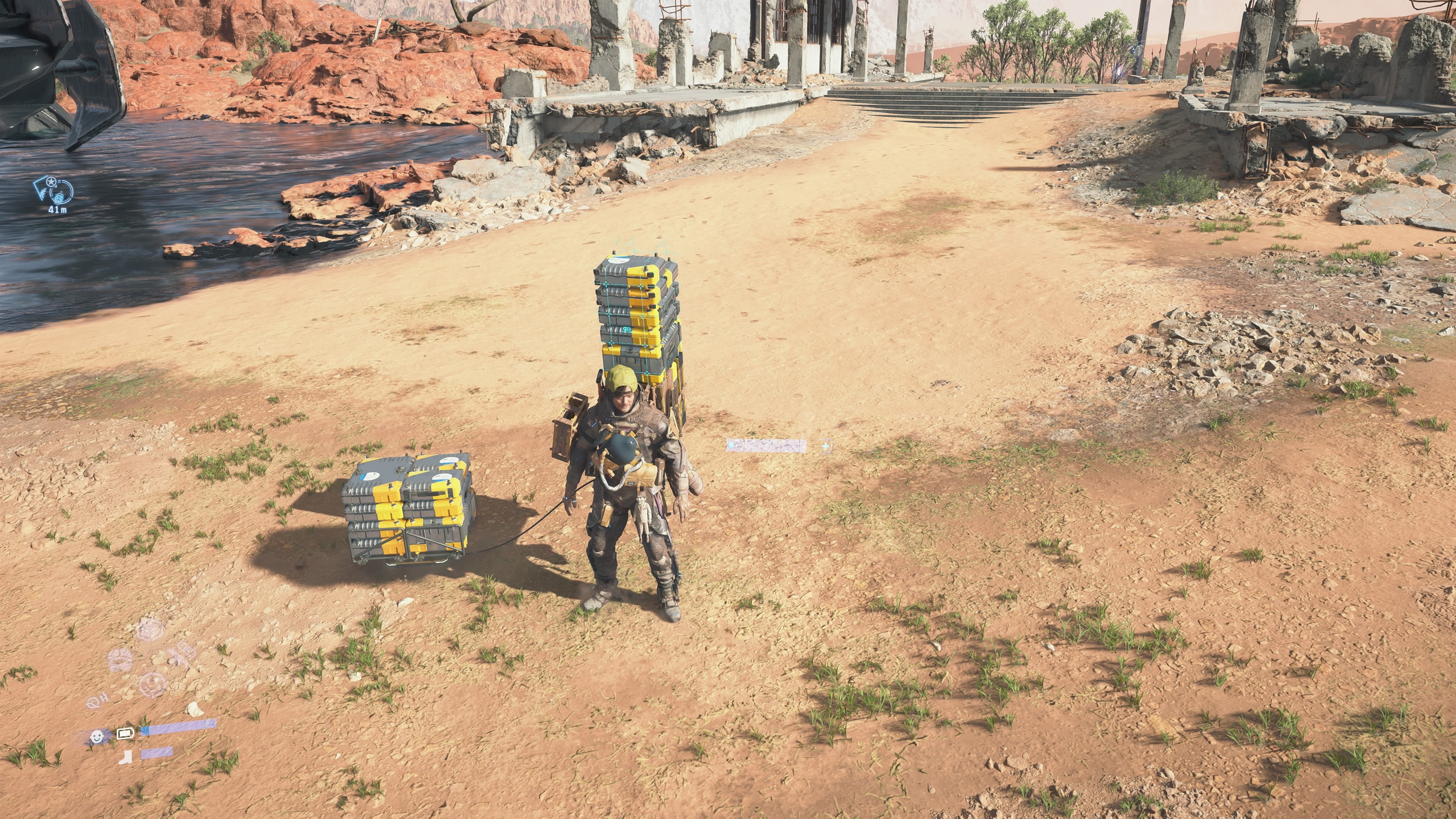 Death Stranding 2 carry capacity: Sam standing in a desert next to a floating carrier holding cargo.