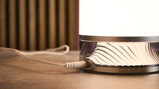 The textured internals of the base of the Govee Table Lamp 2 is lit up white, and the lamp is turned so you can see where the power cable connects to the lamp.