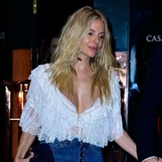 Sienna Miller Styles a white lace top with blue flared jeans.