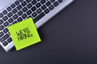 A post-it note stuck to a laptop keyboard reading "We're hiring"