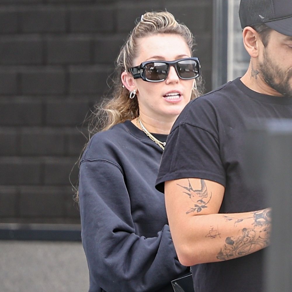 Miley Cyrus wears a black top and black track pants with green trainers and black sunglasses.