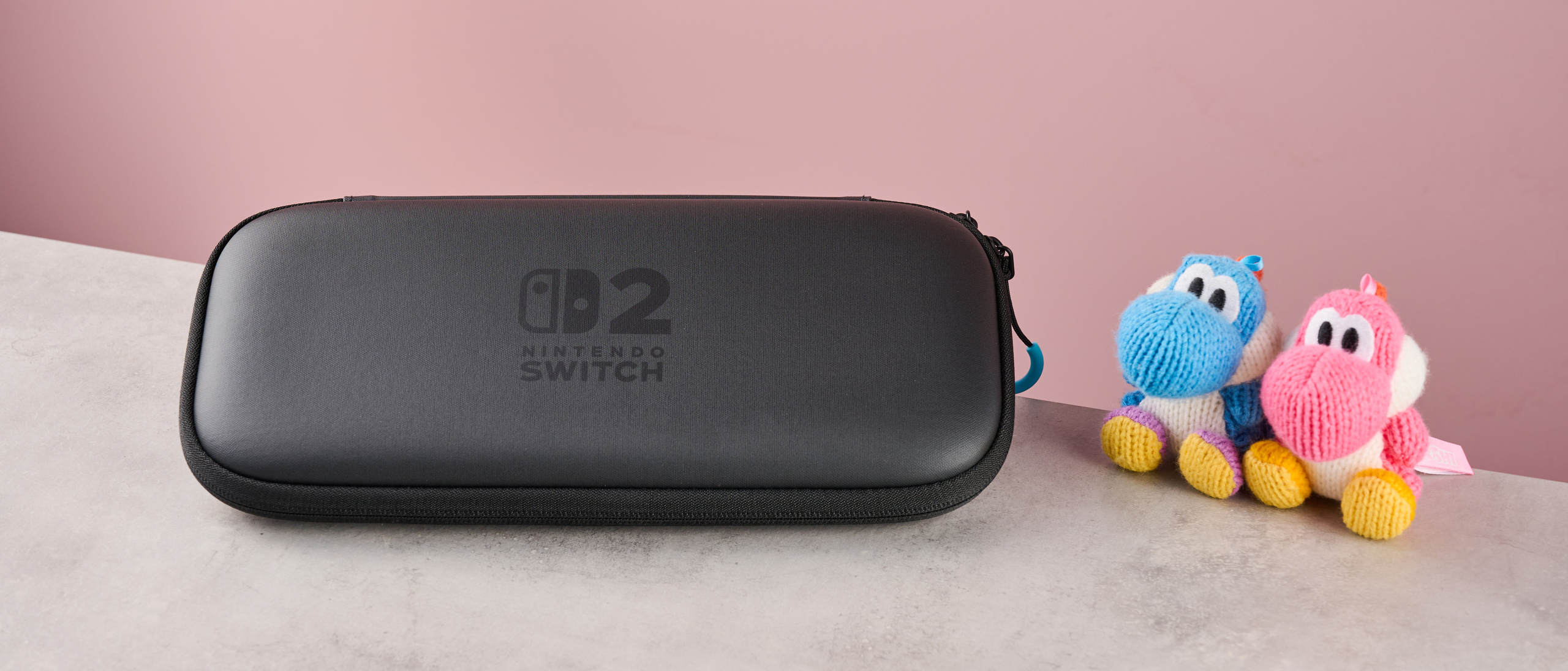 Official Nintendo Switch 2 Carrying Case with a pink and a blue yarn Yoshi amiibo together on the right hand side