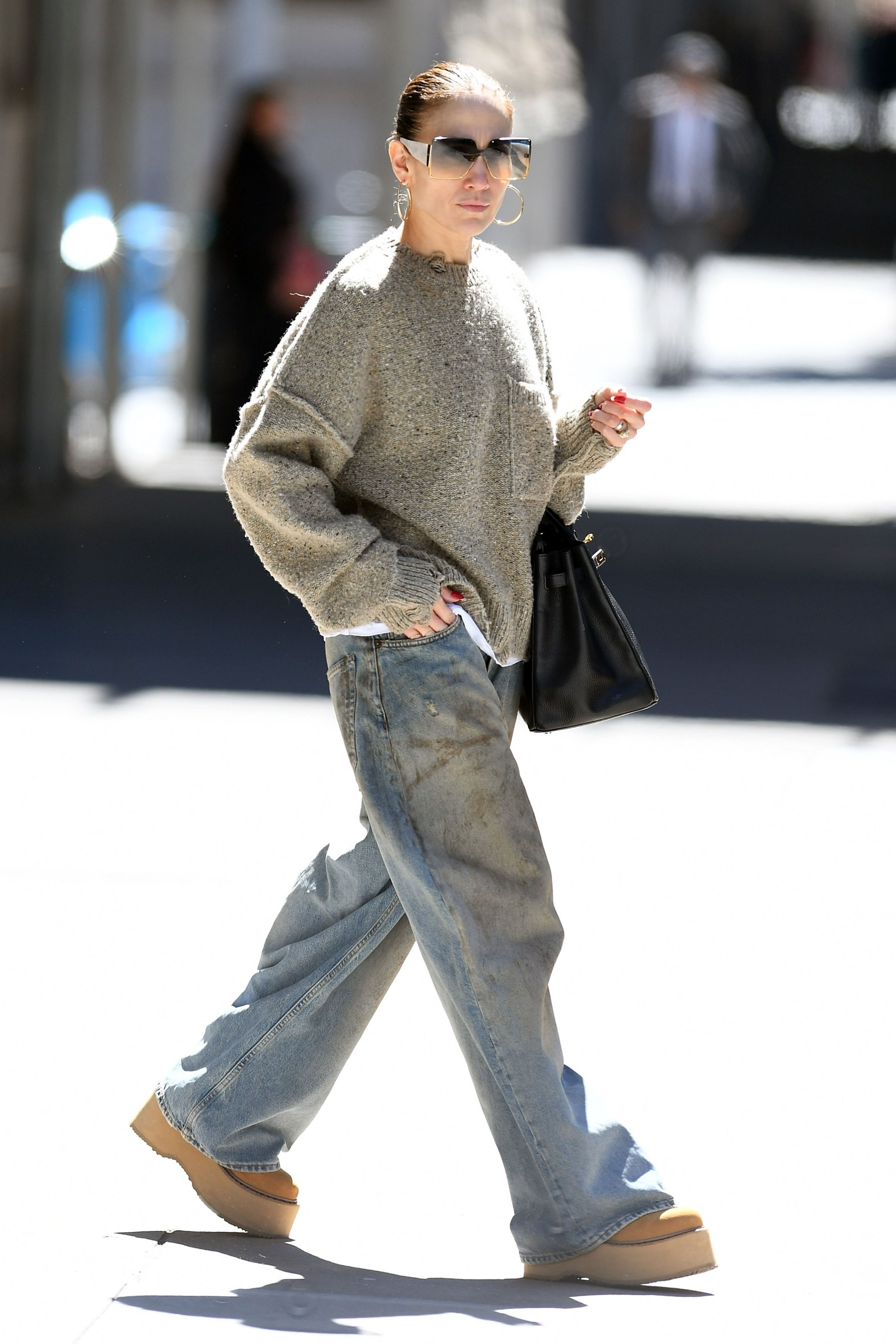 Jennifer Lopez walking on the streets of New York City wearing oversized sunglasses, a slouchy sweater, baggy dirty Acne jeans, and  R13 double stack lace-up boots