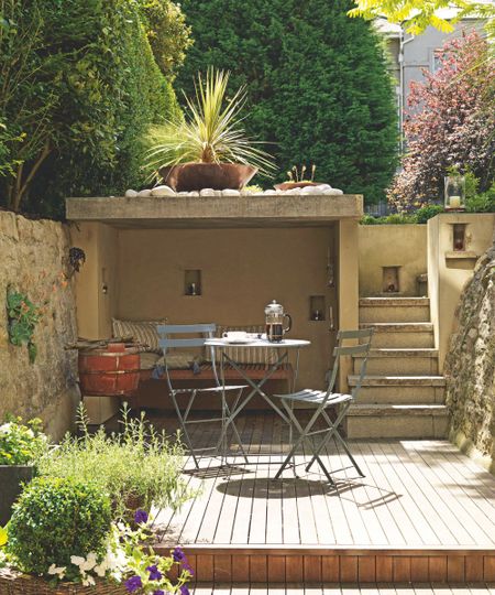 Small patio with stairs leading up to the garden, a level with a wood panelled floor, a metal bistro set, and an alcove with a built-in bench and striped cushions.