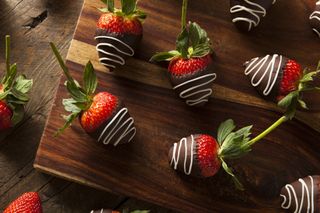Chocolate covered strawberries with white chocolate drizzle on a wooden board.