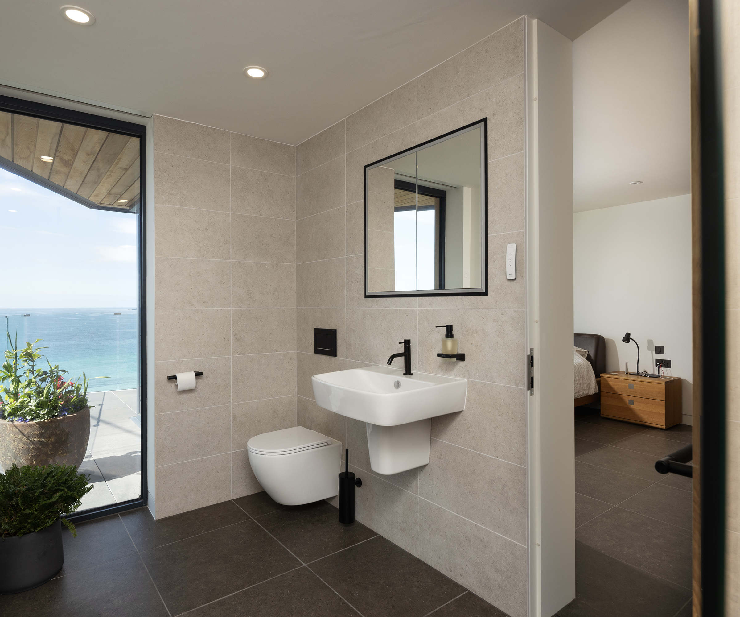 A large ensuite attached to a bedroom with light tiling and black fixtures