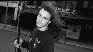 Death's Chuck Schuldiner holding a guitar in the street in New York