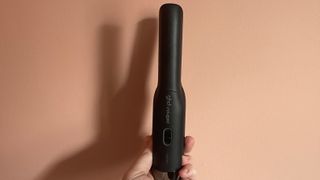 The GHD Unplugged being held vertically against a coral background