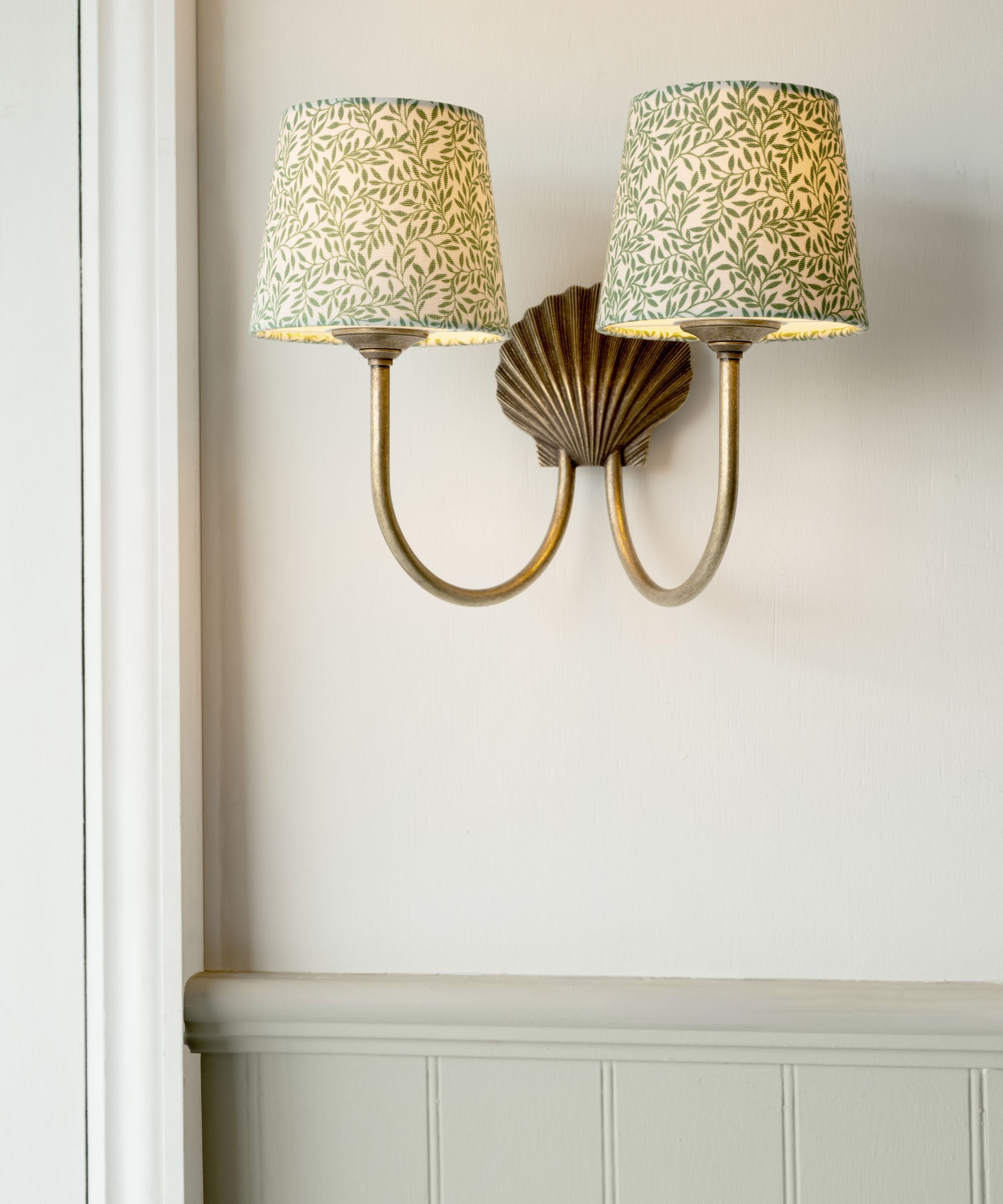 A wall scone light in brass with two green floral patterned lampshades