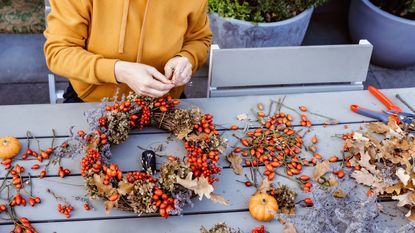 Woman Sitting On Table creating a wreath out of autumn flowers and berries