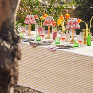 garden table with stripe tablecloth, rechargeable table lamps, green glassware, stripe napkins, jugs of poppies