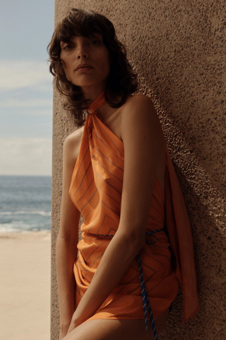 A Maggie Marilyn wears an orange dress in front of the ocean