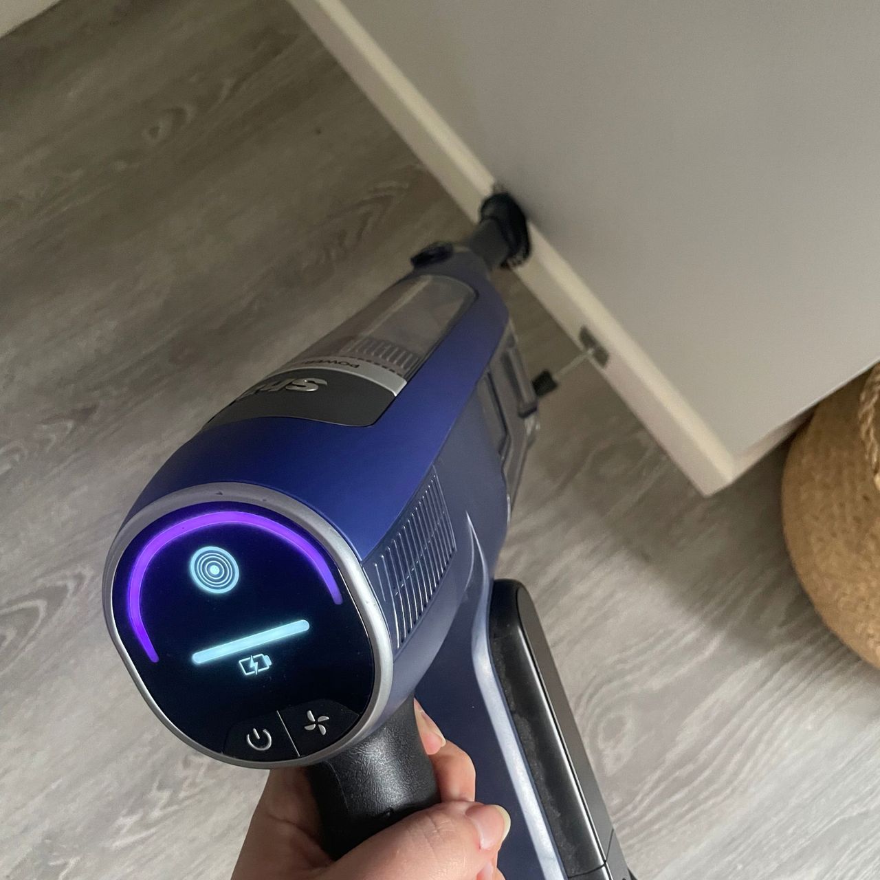 Using a Shark vacuum to dust white skirting boards in a grey painted room