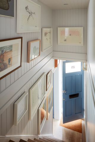 hallway with blue front door and panelled wall and framed photographs