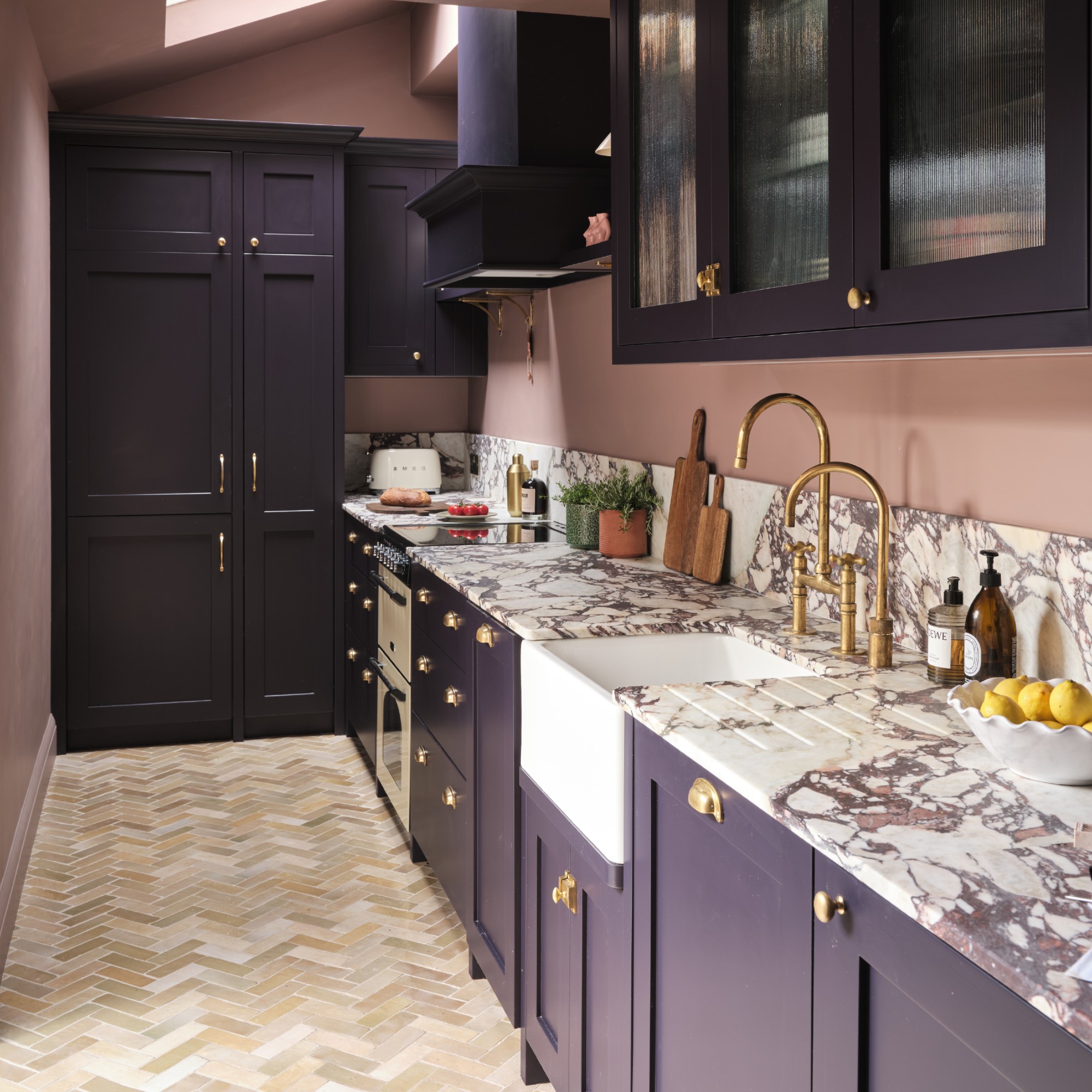 A narrow kitchen with dark purple-painted cabinets and earthy pink walls