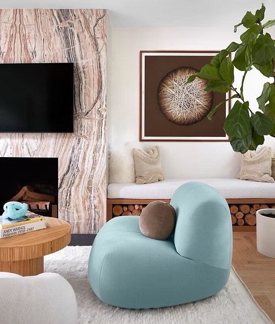 Cara Woodhouse's living room with art on the wall, a statement fireplace with a tv attached and a pale blue modern accent chair