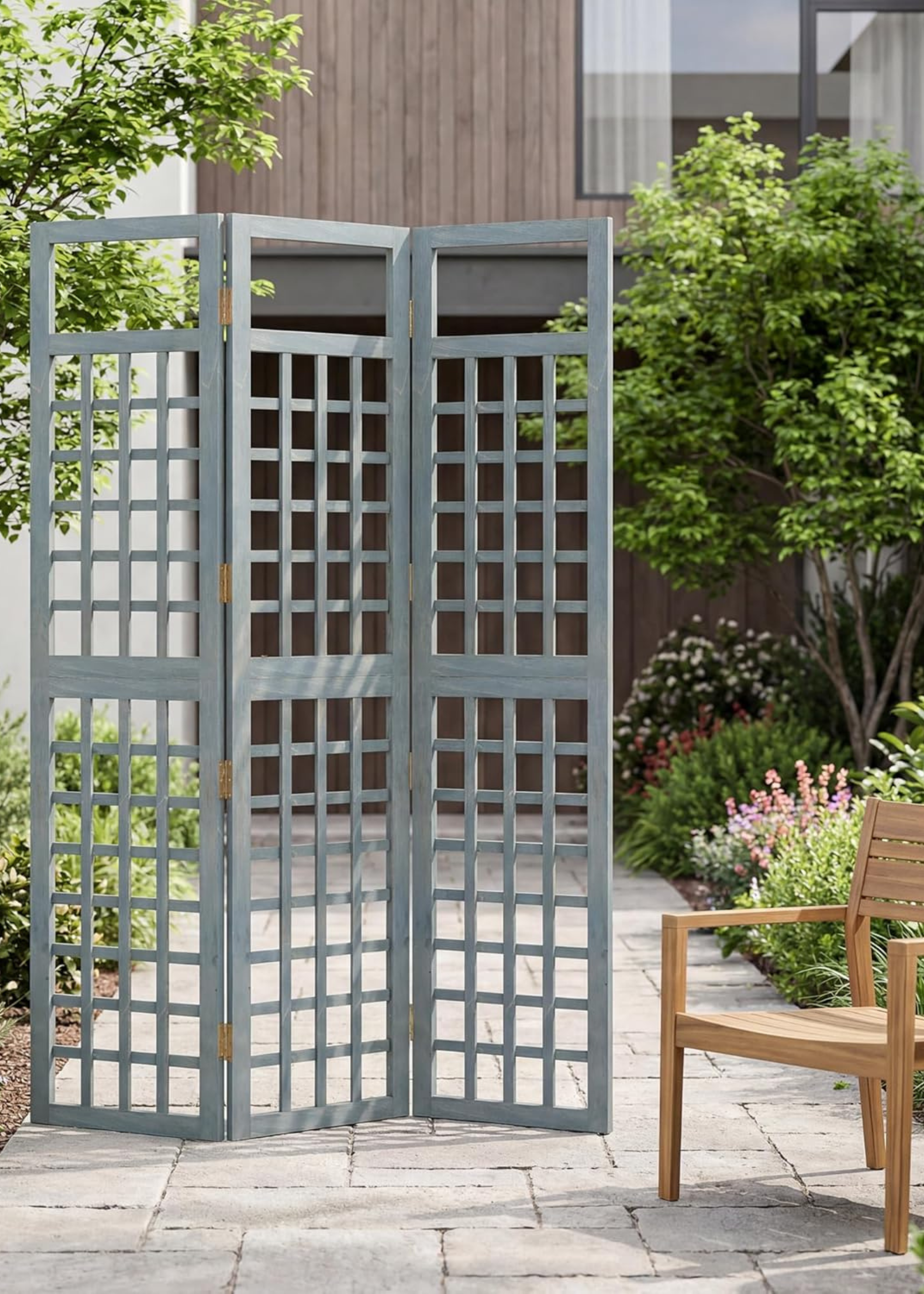 OUTSUNNY's Foldable Outdoor Privacy Screen next to a wooden chair in front of a modern home, with flower beds lining the stone and trees either side