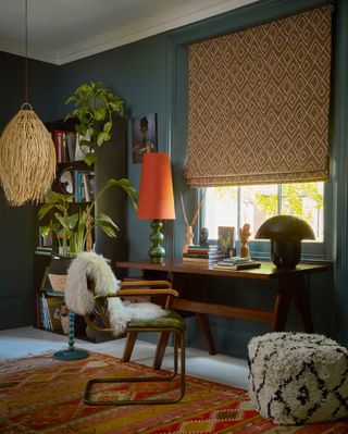 A colourful study with blue walls and an orange geometric patterned roman blind