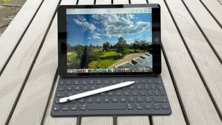En iPad 10.2 (2021) står ute på ett träbord med ett tangentbord och en stylus.