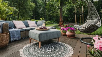 An outdoor backyard with sofas, plant pots, an outdoor rug, and comfy chairs