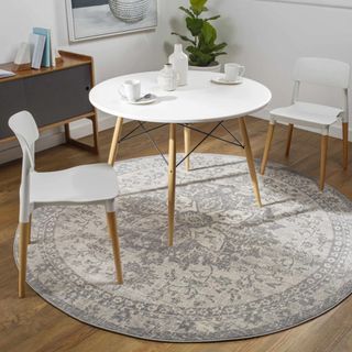 A gray vintage round rug sits underneath a white and wooden dining room table