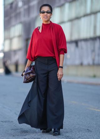 Tamu McPherson wearing black sunglasses, silver earrings, a dark brown Cos Pillow Quilted Clutch handbag and a slouchy red jumper.