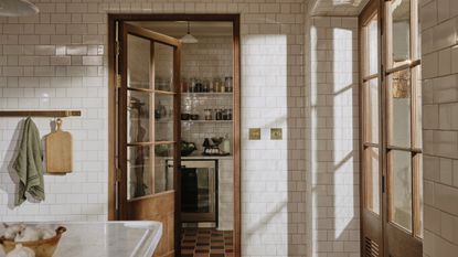 A traditional kitchen with white tiles walls with a glazed wooden door into the walk-in pantry