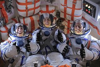 three people in spacesuits give thumbs up while laughing