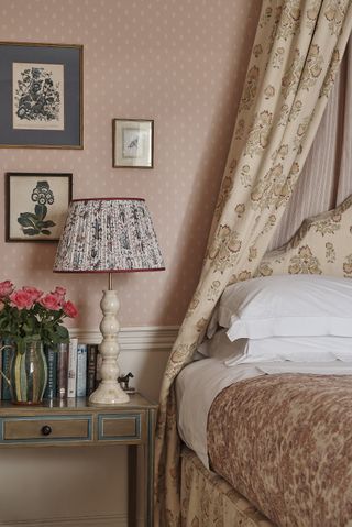 Pink/peach traditional bed and bedside table with floral fabrics including on a lamp, illustrating how to make a small bedroom look bigger