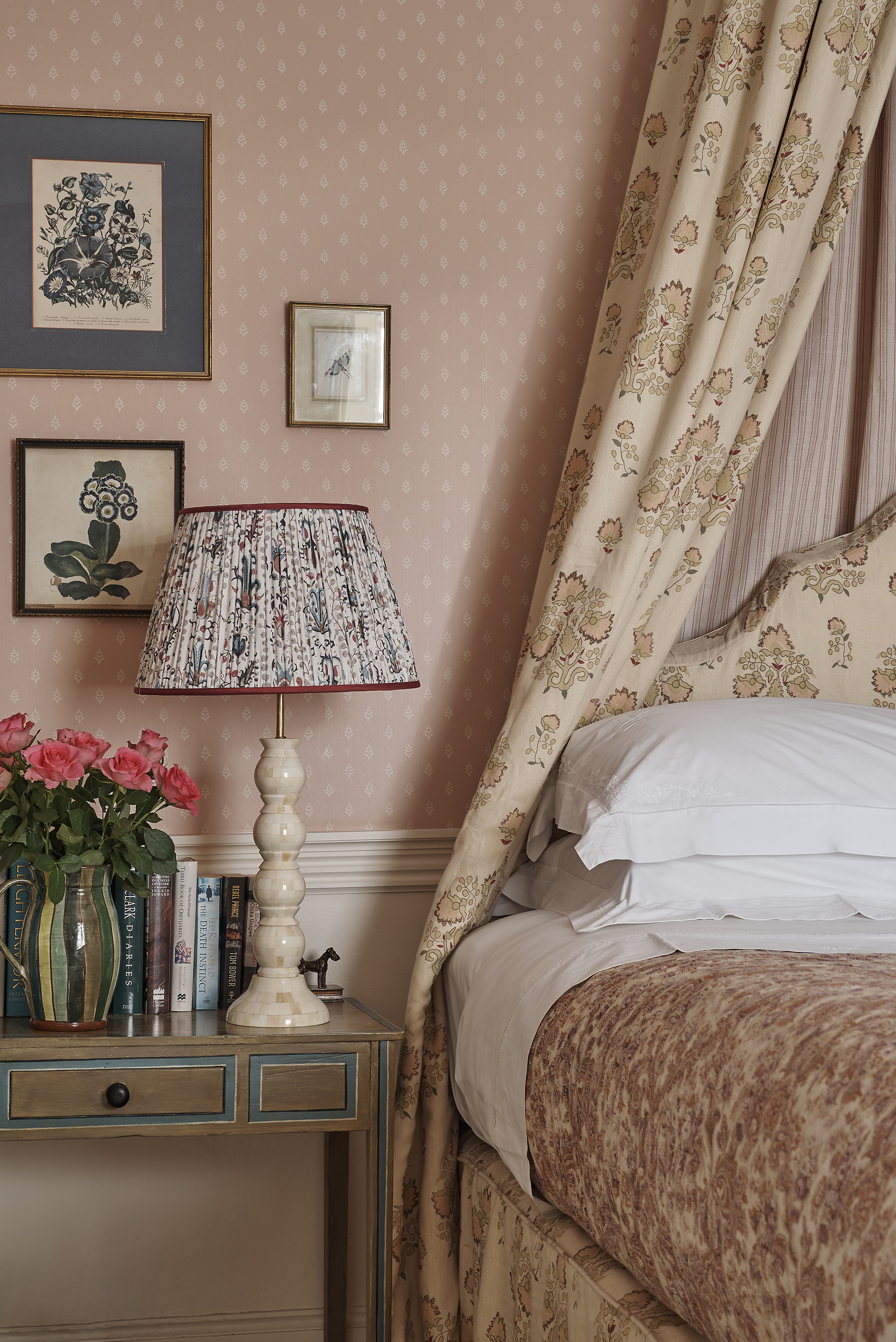 Pink/peach traditional bed and bedside table with floral fabrics including on a lamp, illustrating how to make a small bedroom look bigger