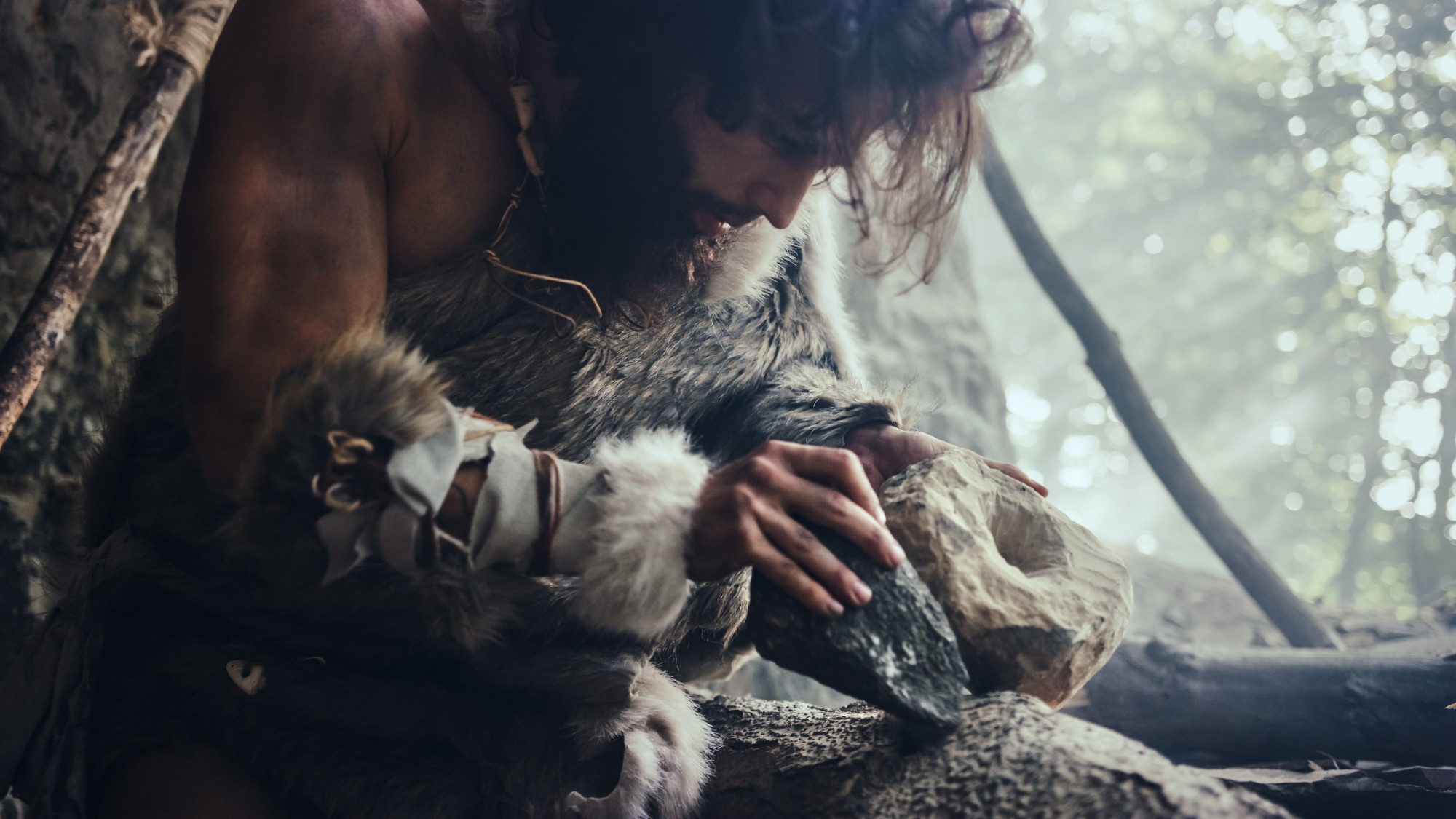 A prehistoric man sharpens a stone tool.
